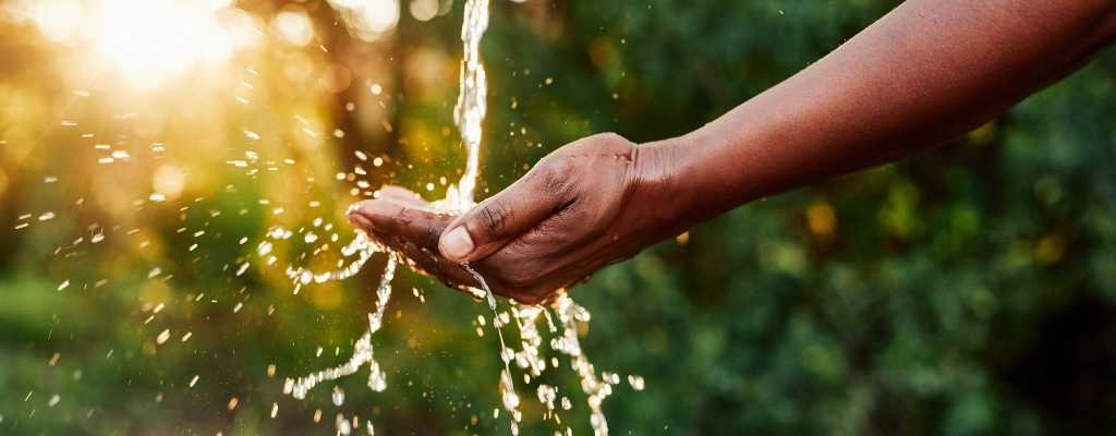 Water being poured into a hand infront of a blurred hedge 