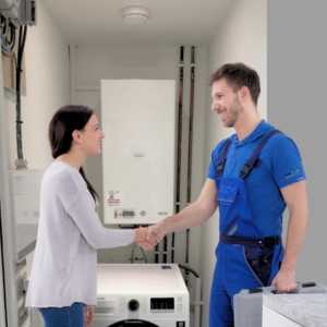 a male plumber shaking a female customers hand infront of a boiler