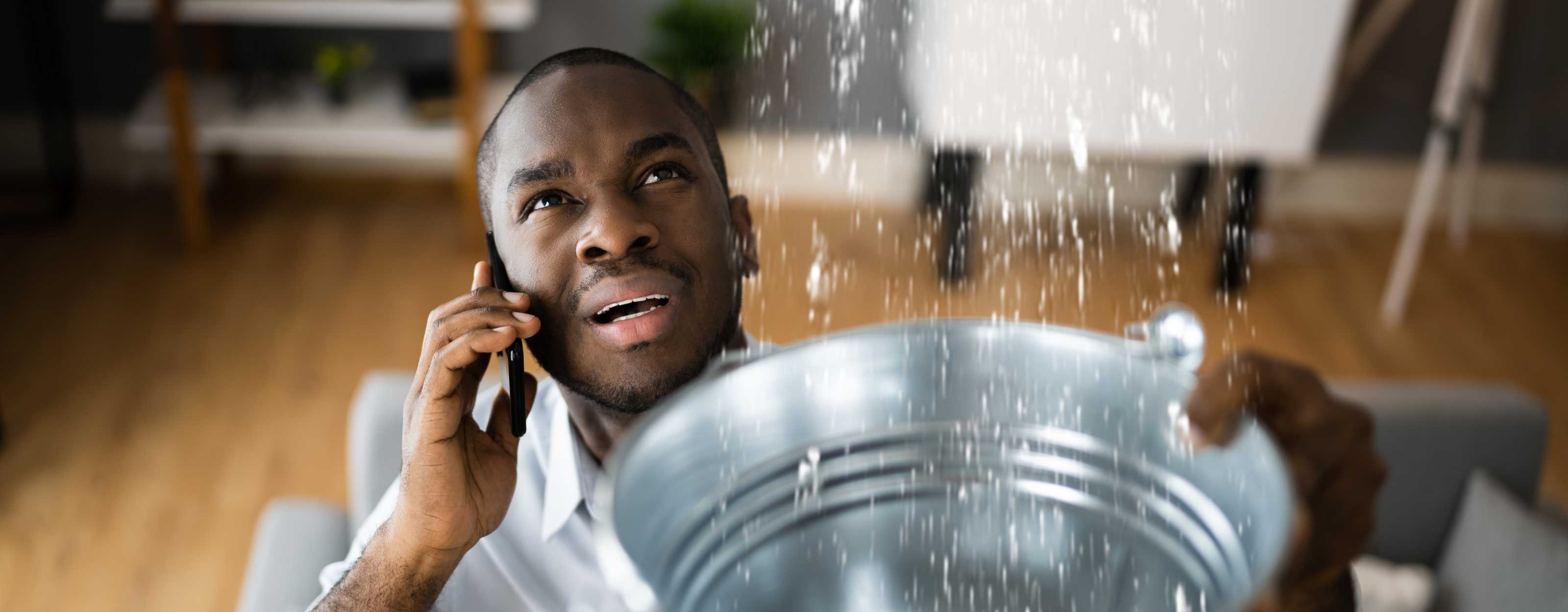 a man with a bucket flling up with water from a leak on the phone