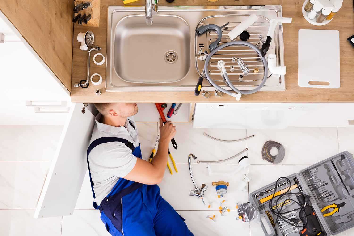 Plumber Working underneath Kitchen Sink with Tools Spread across The Floor