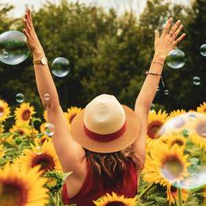Woman in Sunflower Field Raising Hands in Air with Bubbles