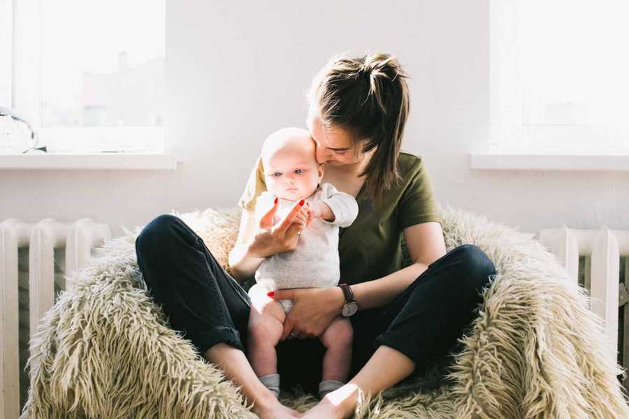 Woman Holding Baby Sitting Next to Radiator