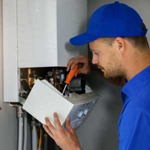 a male plumber in a blue cap using a screwdriver in a boiler