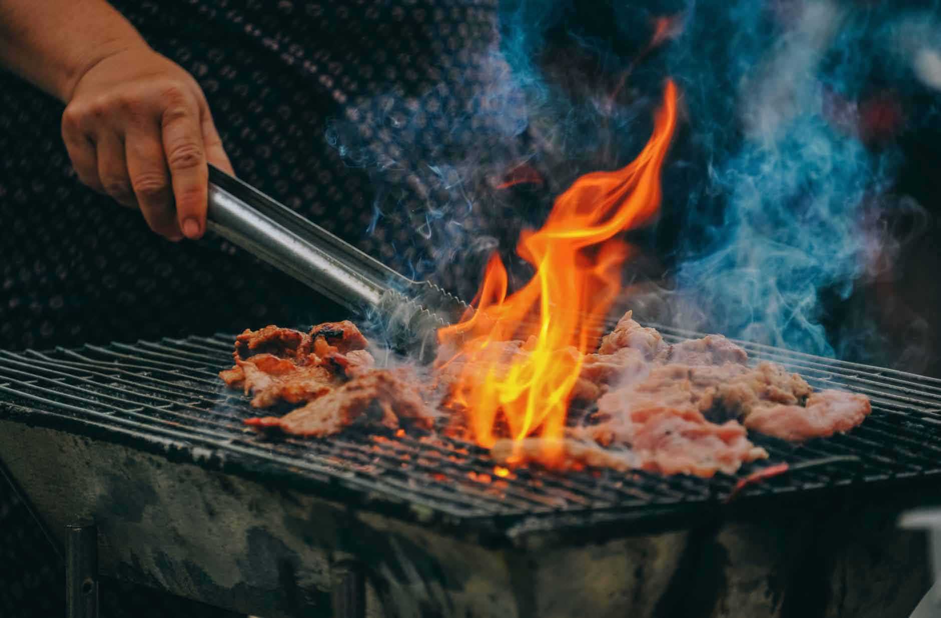 Fire Coming through Barbecue as Man with Tongs Turns The Meat