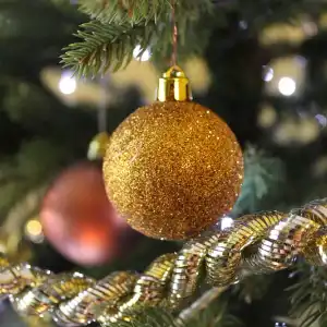 Gold glittery Christmas bauble hanging from Christmas tree branch above golden tinsel