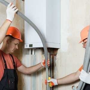 Two plumbers using foam to insulate the pipes attached to a boiler