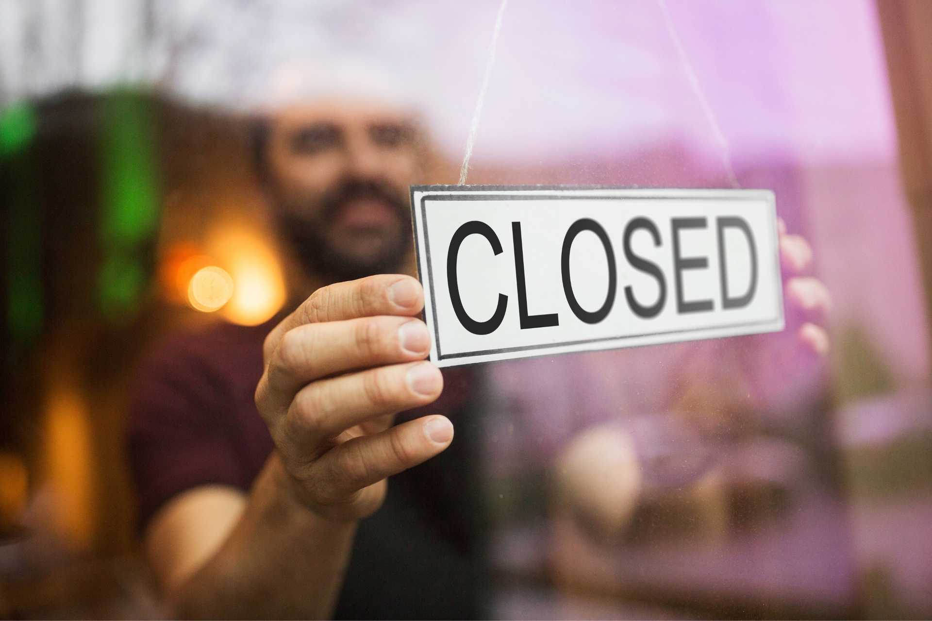 Man Hanging a Closed Sign on a Shop Door