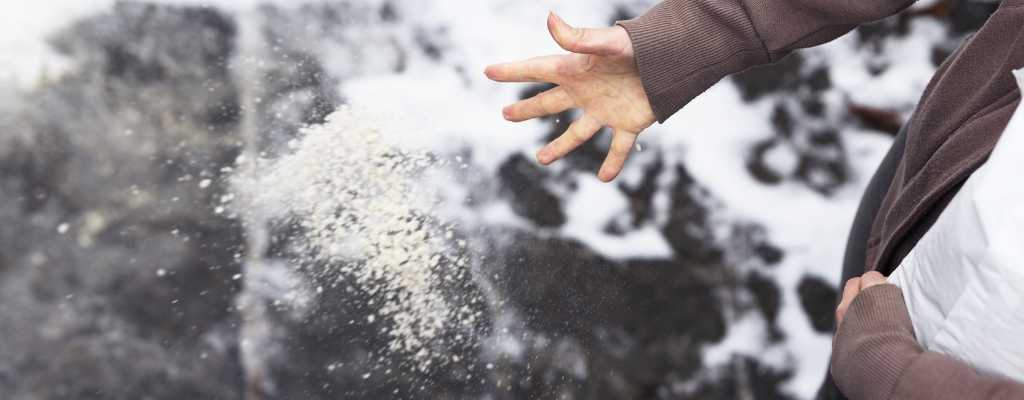 persons hand throwing salt down to avoid ice