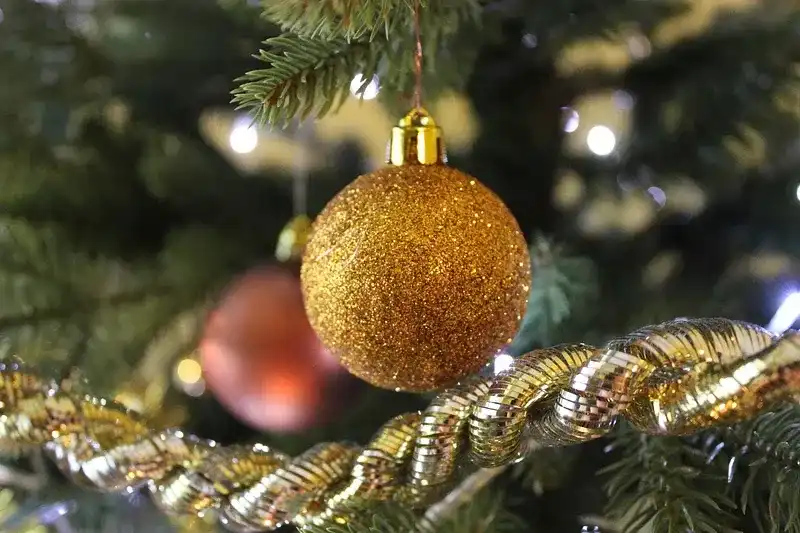 Gold glittery Christmas bauble hanging from Christmas tree branch above golden tinsel
