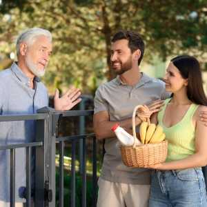 an older man talking to a young couple over a gate